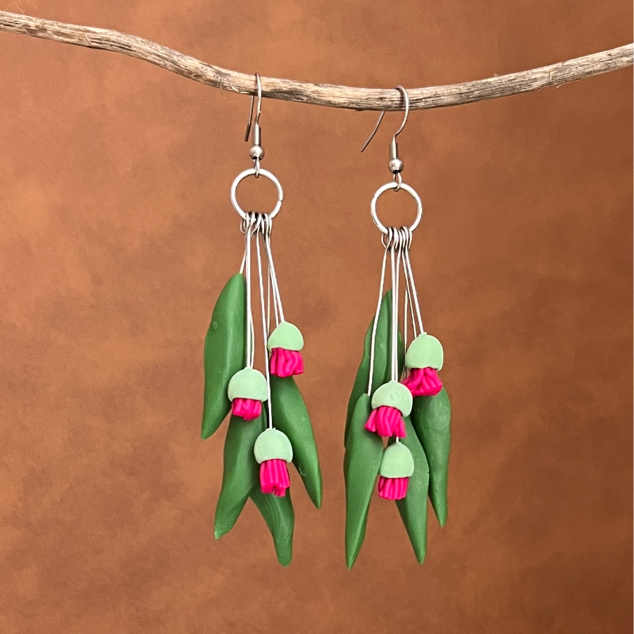 Clay earrings made to look like gum leaves and Pink blossoms hanging on a stick with a leather background