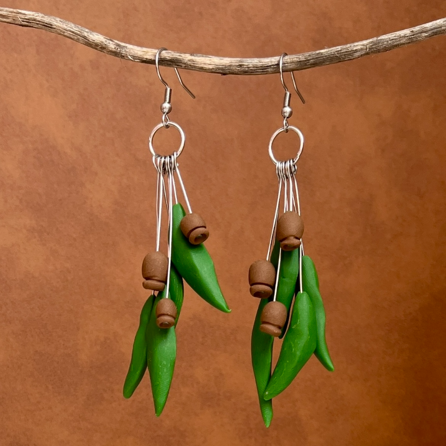 Clay earrings made to look like gum leaves and gum nuts hanging on a stick with a leather background