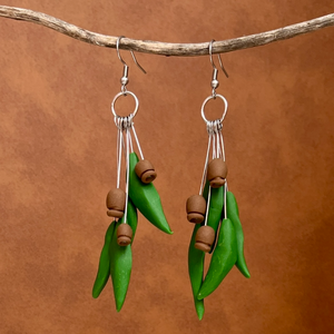 Clay earrings made to look like gum leaves and gum nuts hanging on a stick with a leather background