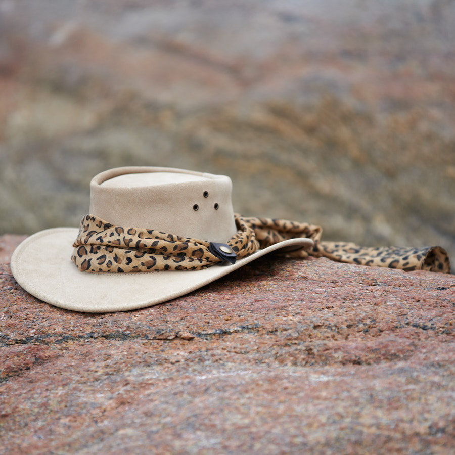 The Jillaroo cowhide suede hat by Jacaru Australia in sand colour with a leopard look design brown scarf on the crown of the hat that hangs over the back of the hat displayed on a rock